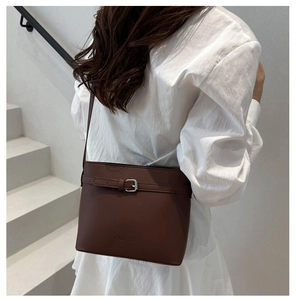 Détail du sac seau marron foncé avec boucle argentée et logo porté par un mannequin