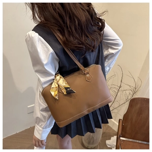 Detail of a brown leather tote bag with silk scarf and white stitching on a model