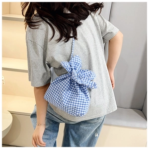 Detail of blue gingham drawstring bucket bag worn on shoulder by model in casual style