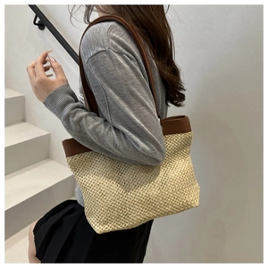 Détail d'un sac cabas en paille tressée avec bandoulière en cuir marron porté à l'épaule