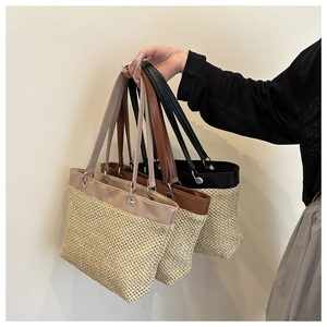 Three colors of woven straw tote bags with leather shoulder straps and metal hardware