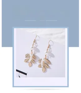 Dettaglio di orecchini a foglia barocca dorata con perle bianche e delicato design a foglia
