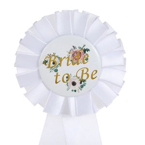 Detail of white satin Bride to Be badge with gold lettering and floral patterns