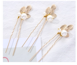 Close-up of golden leaf hair pins with white pearls on a minimalist white fabric background