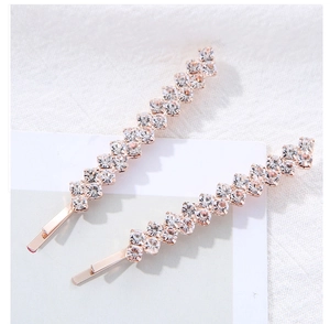 Détail de deux barrettes en or rose serties de rangées de strass géométriques ondulées