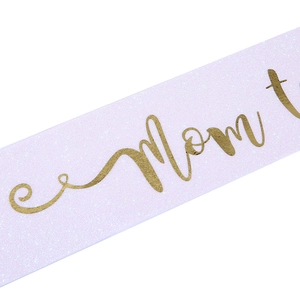 Detail of glitter pink sash with golden Mom to be text and shiny textured finish