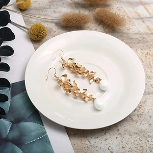 Dettaglio di orecchini a forma di orchidea dorata con petali testurizzati e perla a goccia