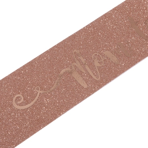 Close-up of glittery rose gold Mom to Be sash with metallic gold foil footprints and lettering