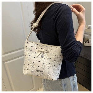 Detailed view of the bow-knot and heart pendant on the cream embossed shoulder bag