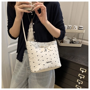 Detail of white bucket bag with black bow patterns and heart pendant in lifestyle setting