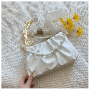 Close-up of white ruched cloud bag featuring large pearl handle and yellow silk scarf strap