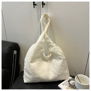 Detailed close-up of white floral embroidery and knotted handle on a soft fabric tote bag