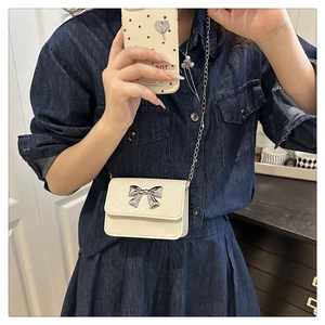 Detail of white mini crossbody bag with silver bow buckle and textured faux leather surface