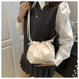 Detailed view of cream pleated crossbody bucket bag worn by model in a modern interior