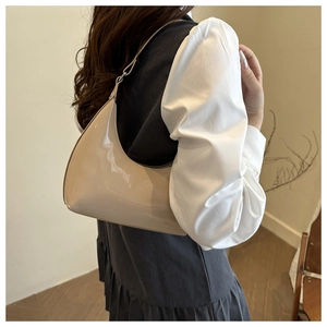 Detail of a beige glossy patent leather hobo bag worn over the shoulder by a model