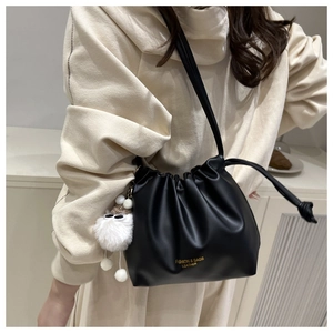 Close-up of black ruched bucket bag with gold lettering and white plush charm detail