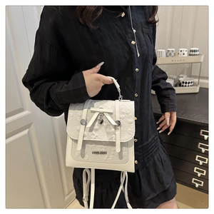 Detail of white leather handbag featuring floral embroidery and heart pendant decoration