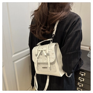 Detail of white lace mini backpack with bow decoration and metal fashion plaque
