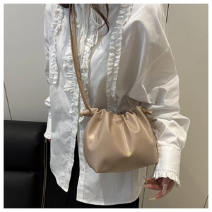Detail of milk tea color pleated drawstring bucket bag with gold designer text
