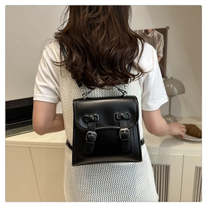 Detail view of a black leather mini backpack with dual buckle closure worn by a model