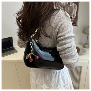 Détail d'un sac porté épaule en cuir verni noir avec charm cerise en métal et zip doré