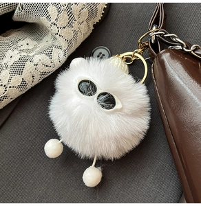 Close-up of white plush monster keychain with sunglasses on a brown leather bag