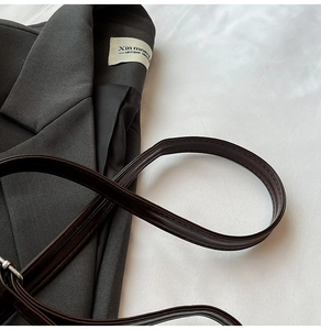 Close-up of a large grey shoulder bag with a polished dark brown leather strap detail