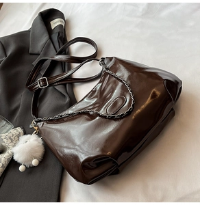 Detail of dark brown glossy shoulder bag with metal chain and soft white pompom charm