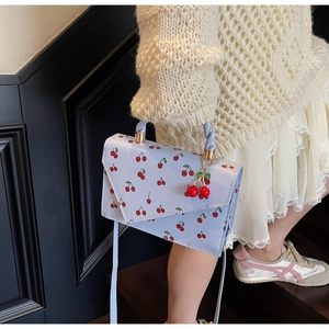 Détail du sac bandoulière bleu clair avec imprimé cerise et breloque cerise en 3D