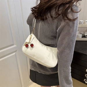 Glossy white hobo shoulder bag with cherry pendant shown on a model in a home setting