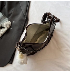 Detail view of glossy dark brown leather shoulder bag with chain strap and fluffy charm