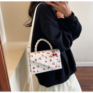 Detail of white cherry print crossbody bag with rope handle and fruit charm