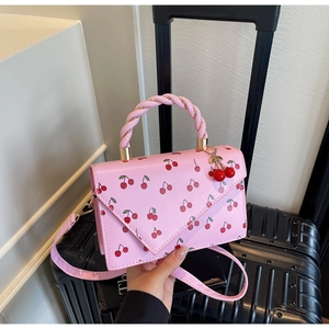 Detail of pink crossbody bag with cherry prints and woven handle on a black suitcase