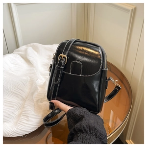 Détail du sac bandoulière en cuir noir brillant avec surpiqûres et boucle dorée