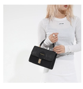 Detail of black leather handbag with sequin flap, gold turn-lock and Fashion lettering