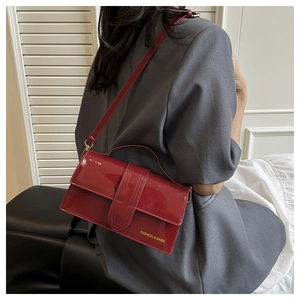 Detail of glossy dark red leather crossbody bag worn by a model in a stylish setting