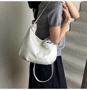 Close-up of a white minimalist shoulder bag featuring a fuzzy charm on a model at a staircase
