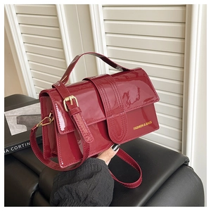 Detail of burgundy patent leather bag with gold buckle and embossed fashion text