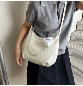 Detail of cream crossbody bag with silver chain strap and soft plush ball charm