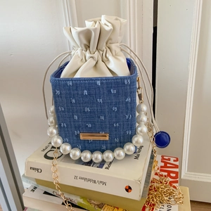 Detailed view of denim bucket bag with pearl handle and cream drawstring closure