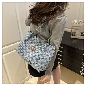 Detail of blue and white plaid denim tote bag with frayed edges and silver chain strap