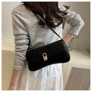 Close-up of black retro shoulder bag with golden lock on model in soft indoor lighting