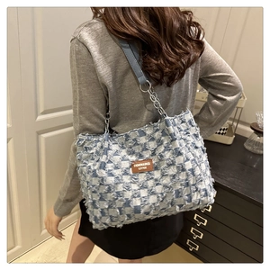 Detail of blue and white checkered denim tote bag with leather label and chain strap