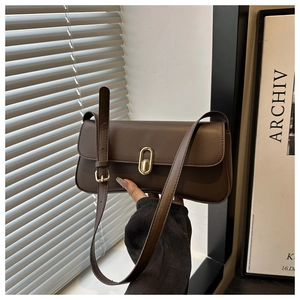 Detailed view of coffee baguette bag with gold buckle held by hand in a chic studio