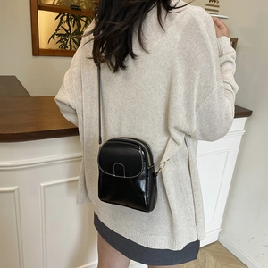 Petit sac bandoulière noir brillant avec surpiqûres blanches porté par un mannequin