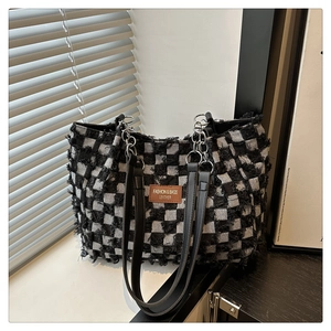 Detail of checkered denim tote with fringe edges, leather patch and silver chain strap