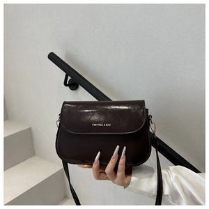 Detail van donkerbruine lederen crossbodytas met merklogo gehouden tegen een trap