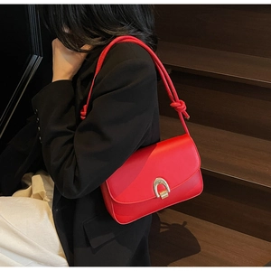 Detail of red leather shoulder bag featuring a gold horseshoe buckle and knotted strap design