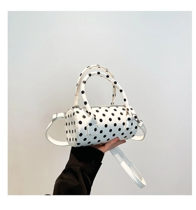 Detailed view of white polka dot cylinder handbag held by hand with shoulder strap
