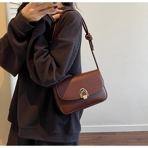 Detail of red-brown crossbody bag with gold half-circle buckle and knotted strap